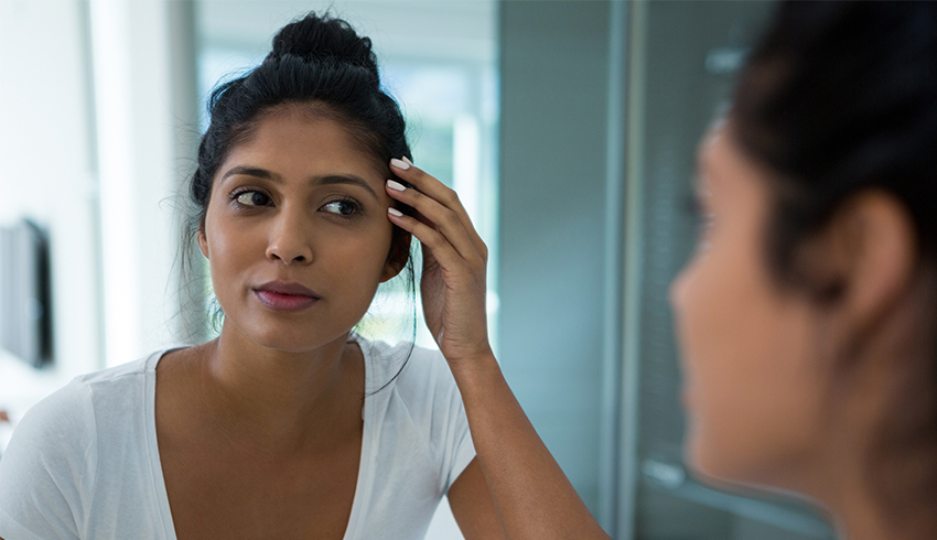 A woman worried about the appearance of her skin looks into a mirror